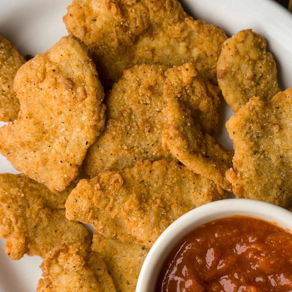 Golden-brown fried chicken tenders with a side of red dipping sauce from The Horseshoe Bar & Grill.