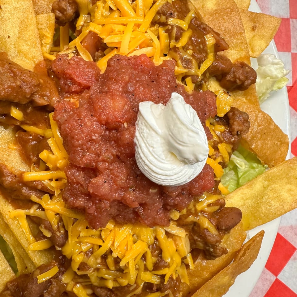 Close-up of chili nachos with shredded cheese, salsa, and a dollop of sour cream.