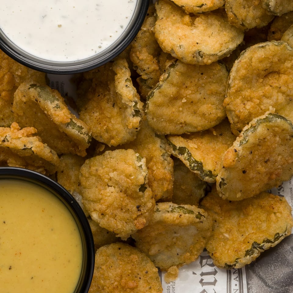 Golden-fried pickle chips with two dipping sauces, one white and one yellow, from The Horseshoe Bar & Grill.