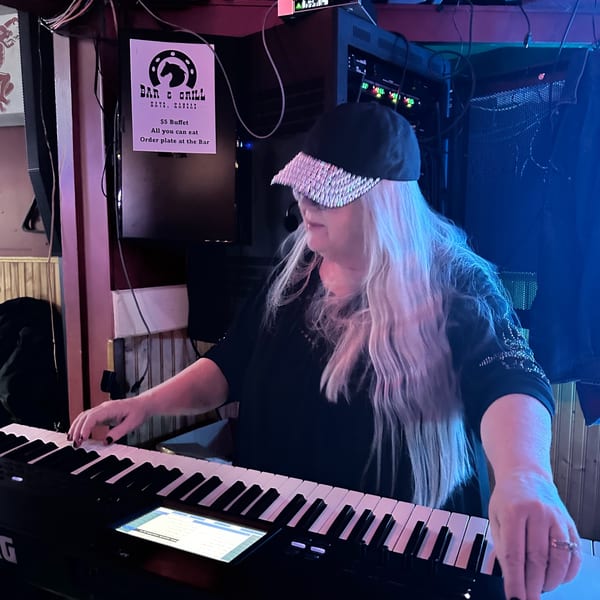 A woman with long blonde hair and a sparkly cap plays a keyboard at The Horseshoe Bar & Grill.