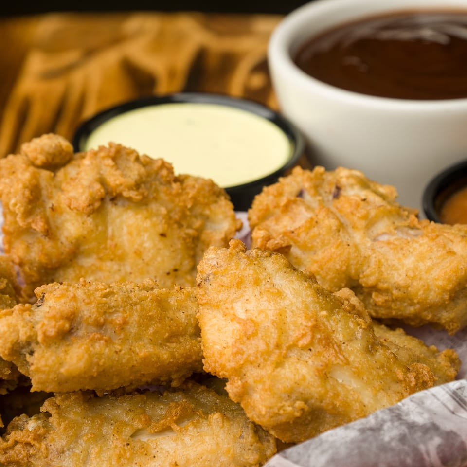 Crispy fried chicken tenders from The Horseshoe Bar & Grill, with dipping sauces in the background.