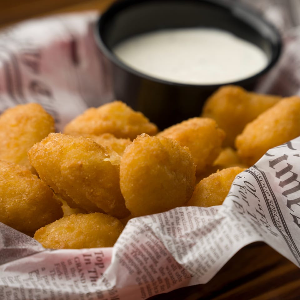 Golden-fried cheese curds in a newspaper-lined basket with a side of ranch dipping sauce.