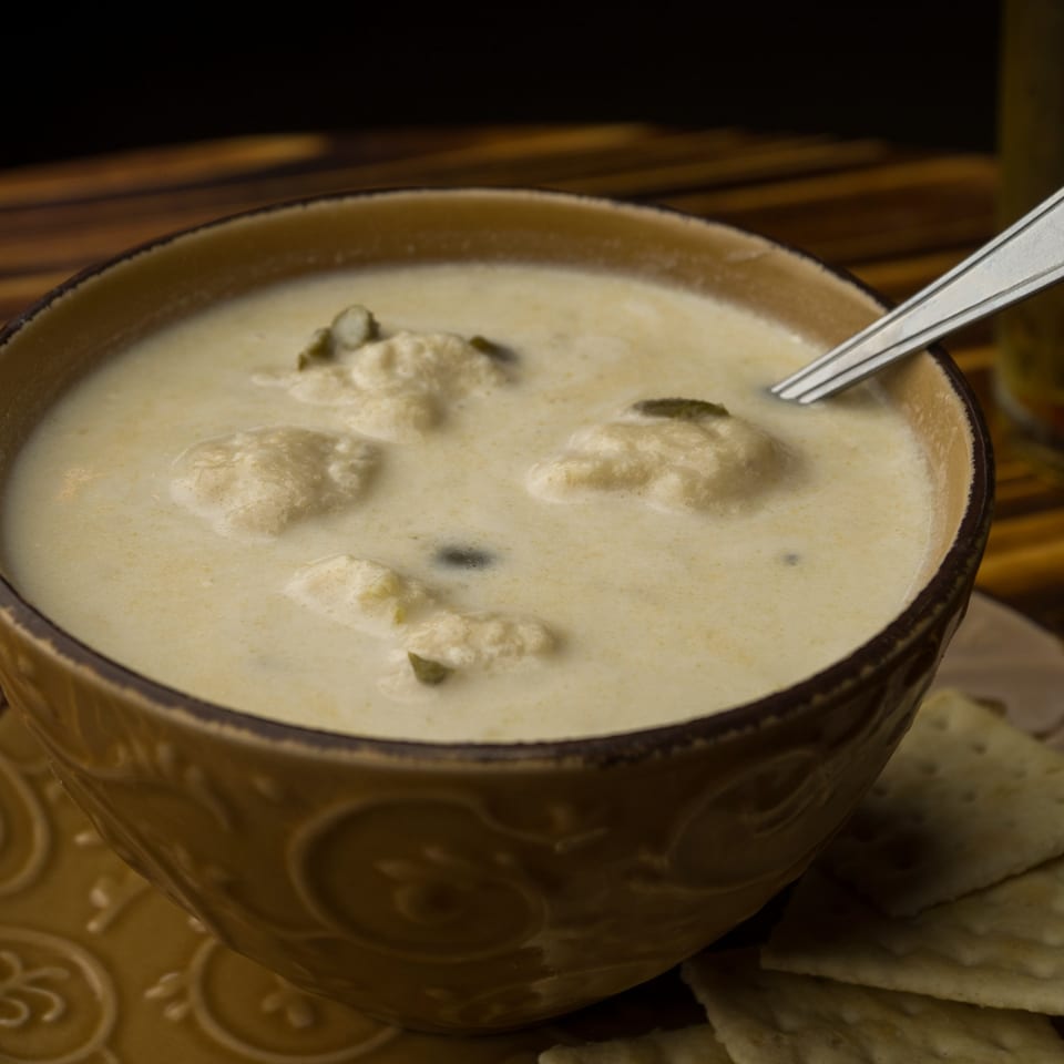Creamy clam chowder in a brown bowl with a spoon and crackers on a wooden table.