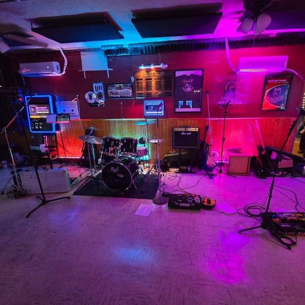 A band's drum set, guitars, and amplifiers on a stage bathed in blue and purple light.