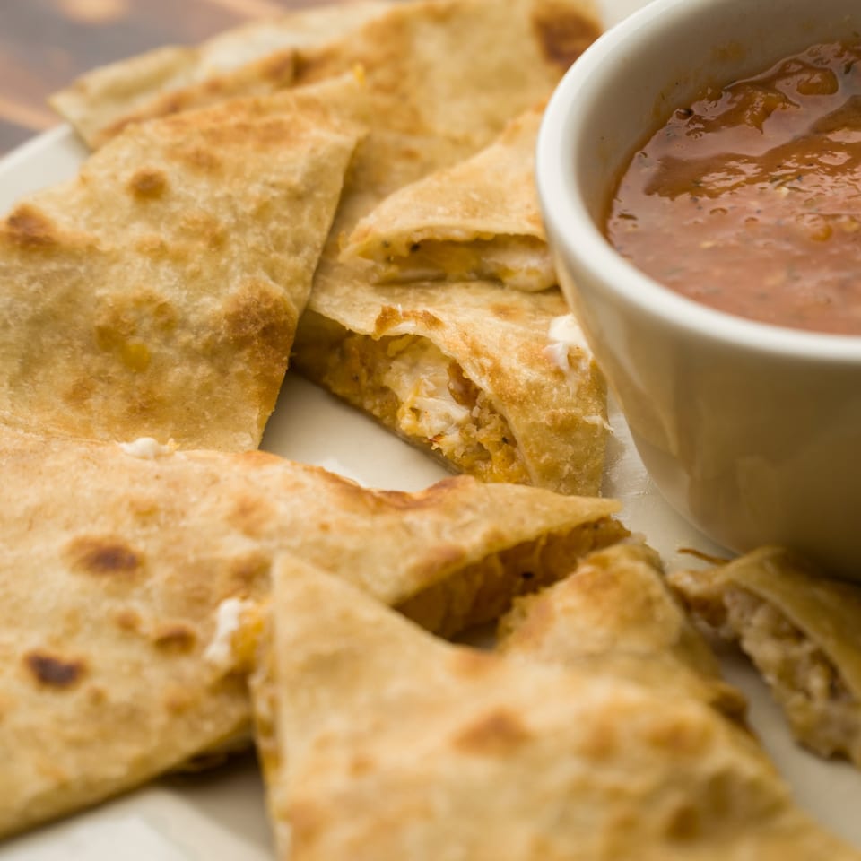 Golden-brown quesadilla wedges filled with cheese and chicken, served with a side of salsa.