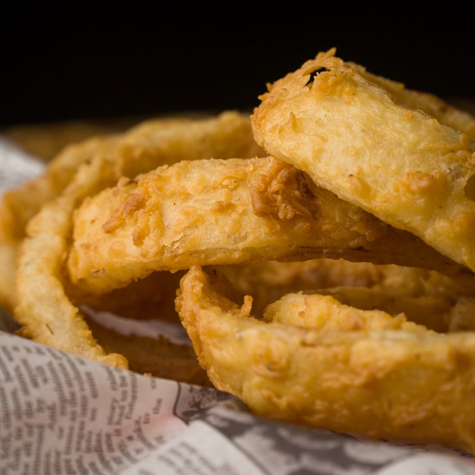 Golden-brown, crispy onion rings from The Horseshoe Bar & Grill, served in paper.