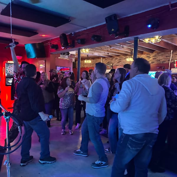 Patrons sing karaoke at The Horseshoe Bar & Grill, illuminated by blue and red lights.