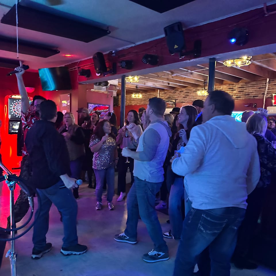 Patrons sing karaoke at The Horseshoe Bar & Grill, illuminated by blue and red lights.