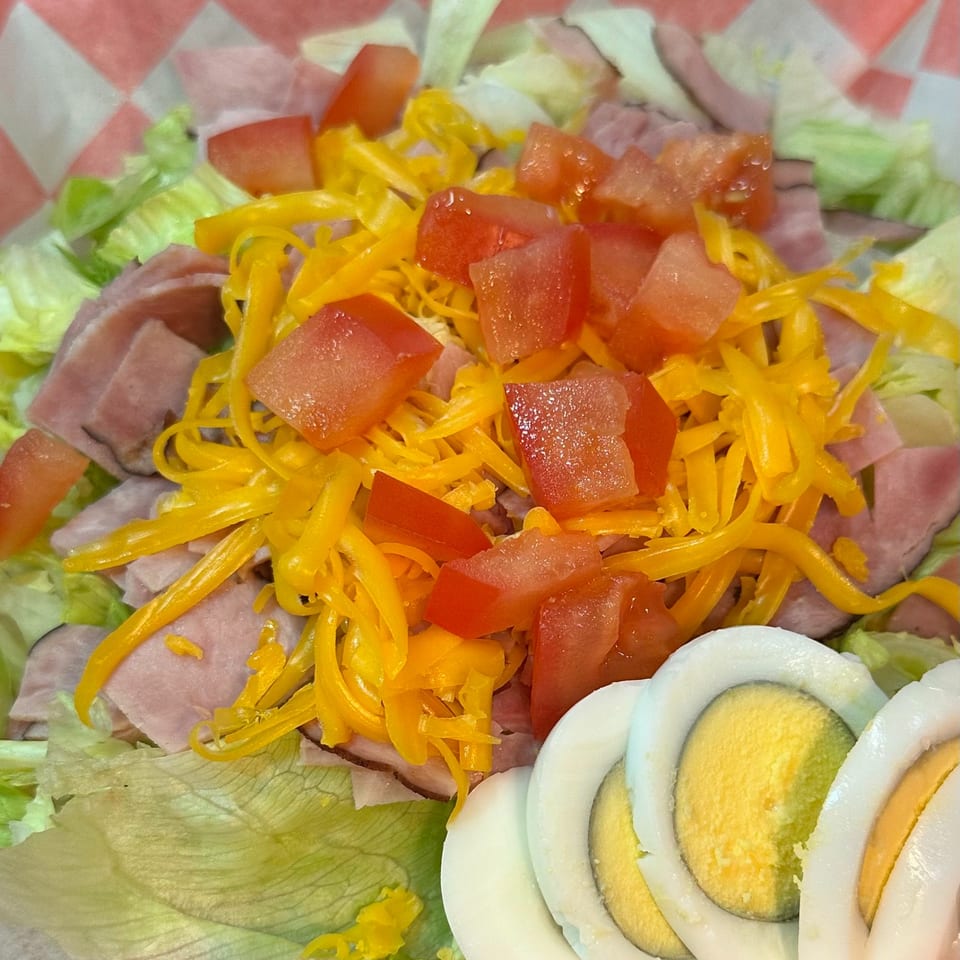 A chef salad with ham, shredded cheese, diced tomatoes, lettuce, and sliced hard-boiled eggs.