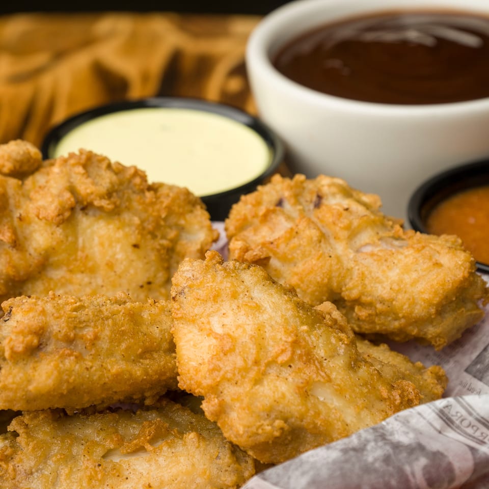 Golden-brown fried chicken tenders with three dipping sauces, including barbecue, at The Horseshoe Bar & Grill.