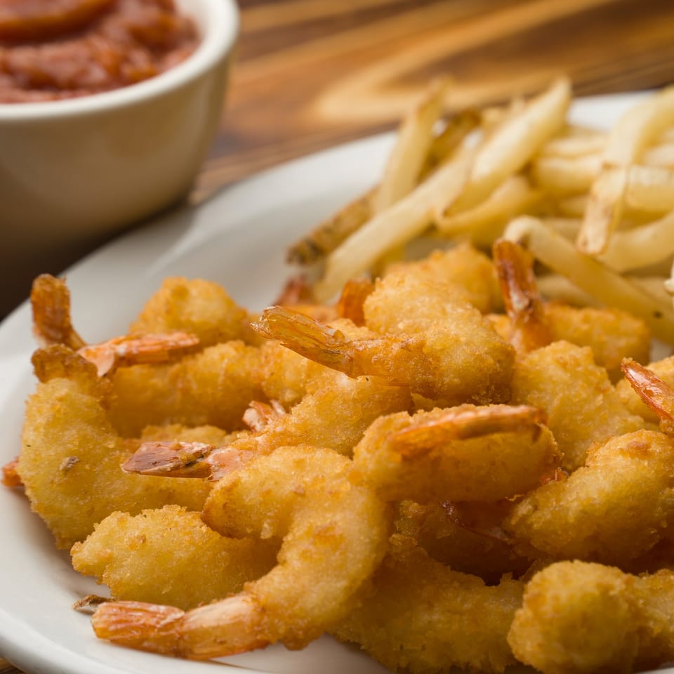 Crispy golden fried shrimp and french fries on a white plate with a side of cocktail sauce.