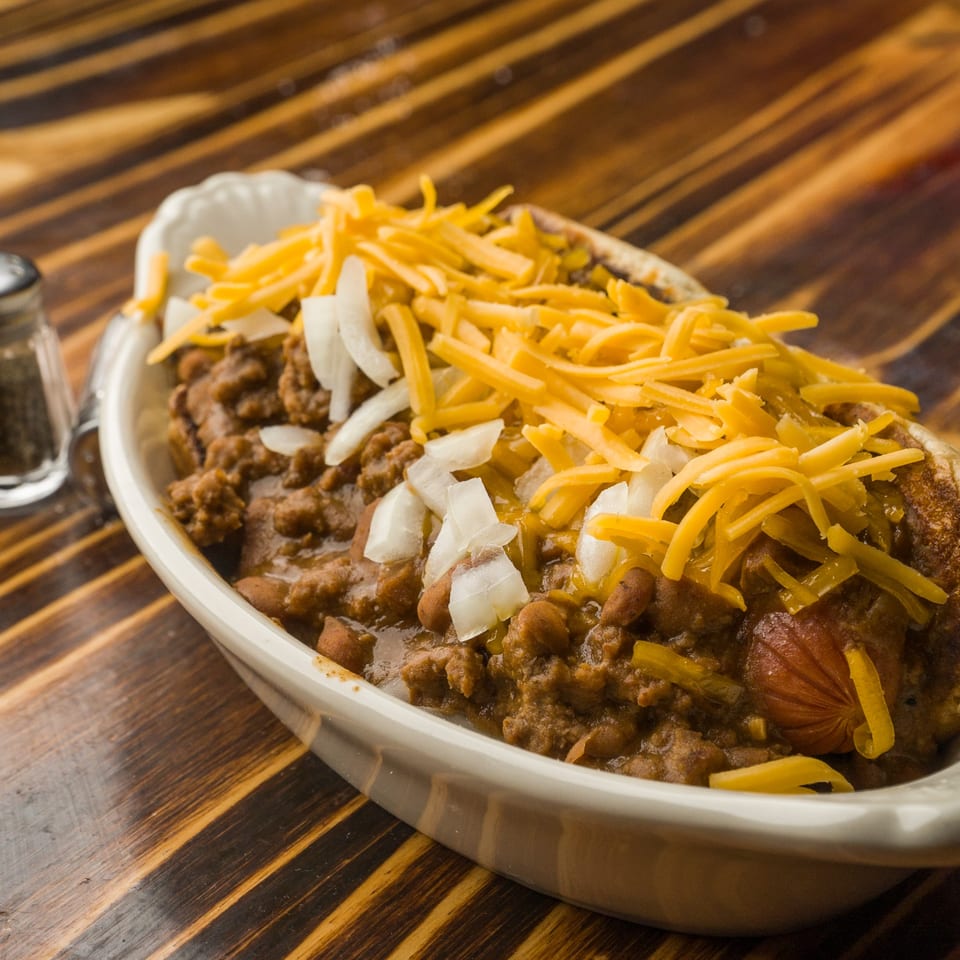 A bowl of chili with shredded cheese and diced onions on a wooden table at The Horseshoe Bar & Grill.