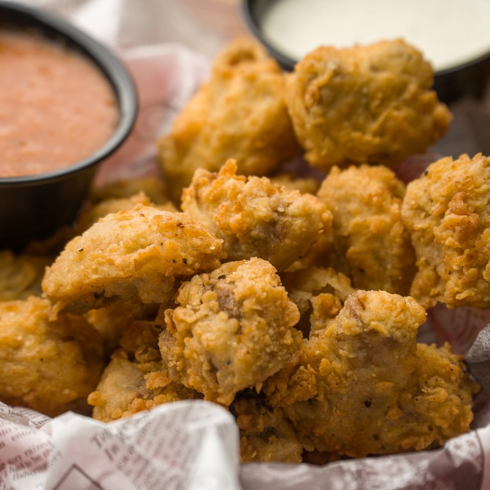 Close-up of golden-brown fried mushrooms in a basket with two dipping sauces.