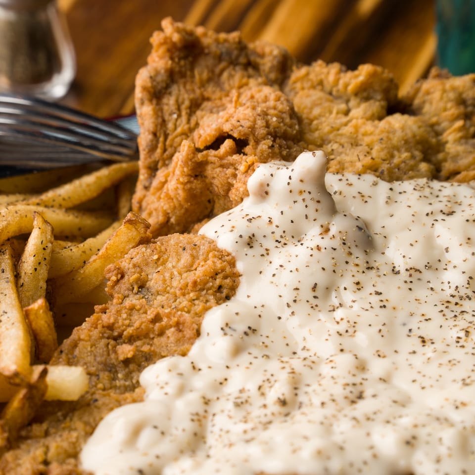 Close-up of golden-fried fish and french fries, generously topped with creamy white gravy and black pepper.