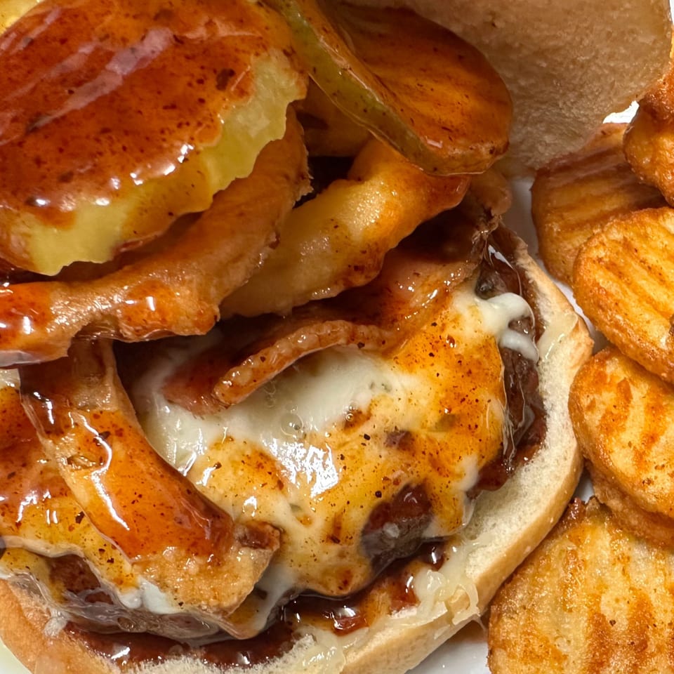 Close-up of a Horseshoe Bar & Grill burger with melted cheese, bacon, and BBQ sauce, served with waffle fries.