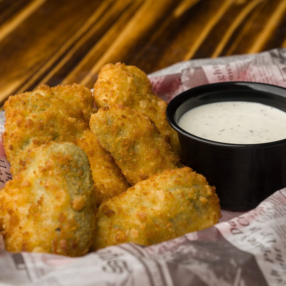 Golden-fried pickle spears and a side of ranch dressing in a basket lined with newspaper.